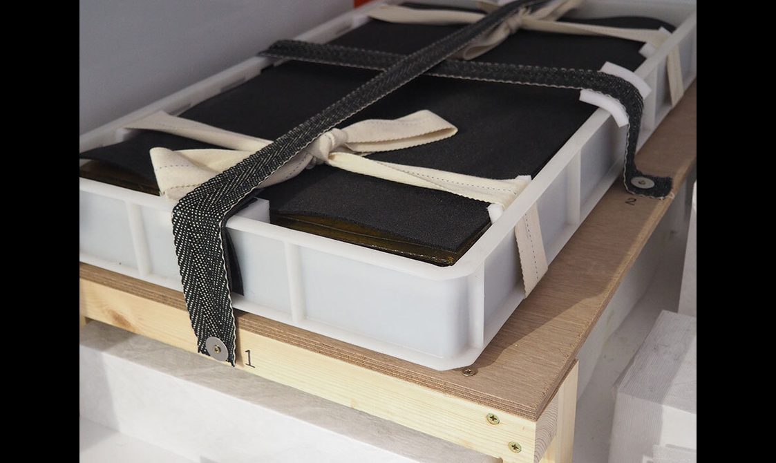 A plastic container holding museum objects strapped into a crate for transport.